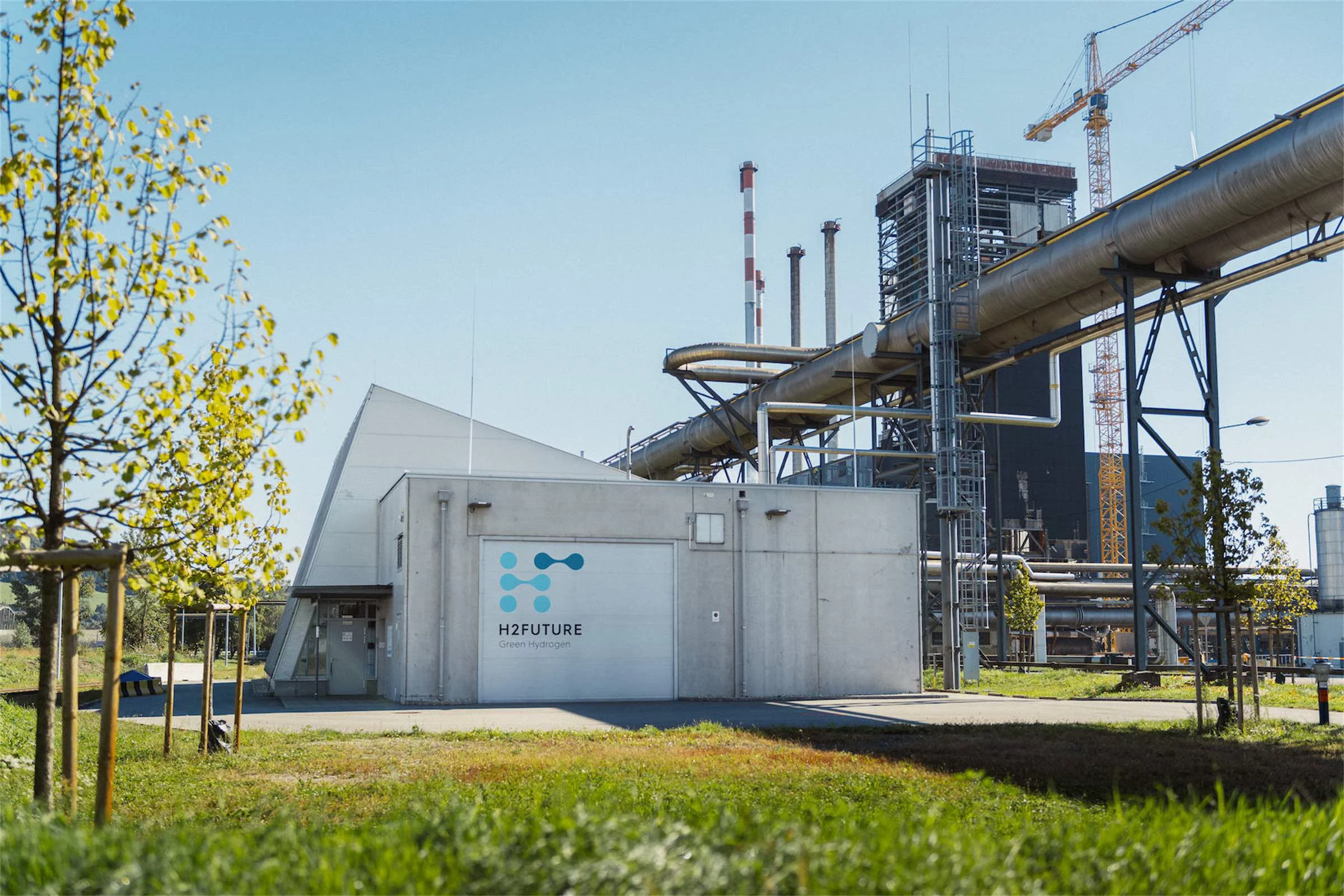 Im Vordergrund eine grüne Wiese, im Hintergrund ein Container mit der Aufschrift H2Future.